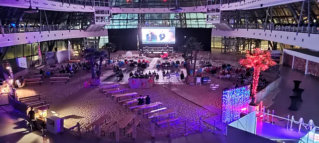 Hala wystawiennicza zamieniona w plażę z kinem letnim, palmami i kolorowym oświetleniem