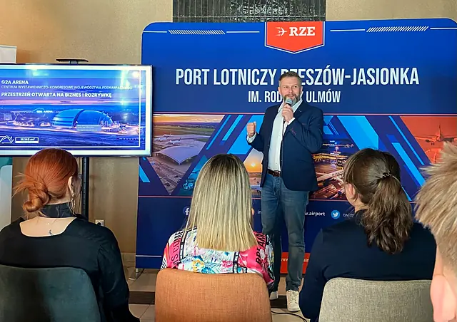 Krzysztof Delikat przemawia do publiczności na tle ścianki Portu Lotniczego Rzeszów-Jasionka